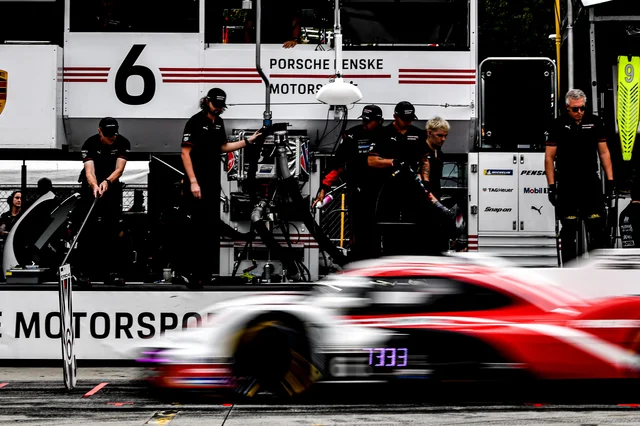 Porsche Penske Motorsport crew in black uniforms working around a refuelling rig in front of the No. 6 transporter at Road Atlanta