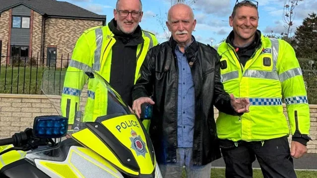 The resident of Meadow Croft care home in Garstang standing between two Lancashire Police officers beside a police motorcycle