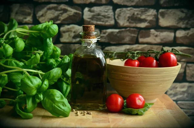 A wide Mediterranean food spread — olive oil, mixed nuts, grilled fish, chickpeas, fresh vegetables — on a terracotta-toned table