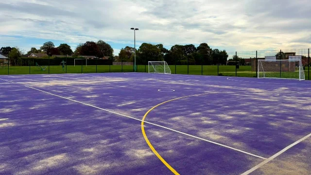 A floodlit purple sports court with white and yellow line markings
