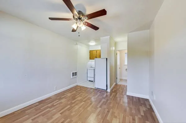 Studio interior at 5471 Vicente Way — light wood floors, ceiling fan, kitchen visible in background
