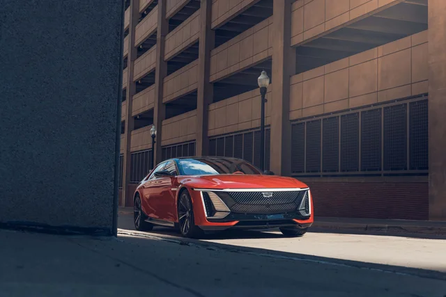 A red Cadillac Celestiq electric sedan photographed from the front on a city street beside a concrete parking structure