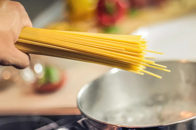 Dried spaghetti submerged in a large pot of boiling water on a kitchen stove