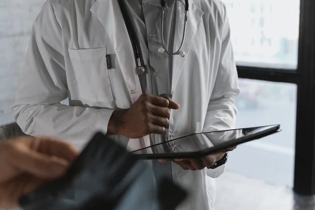 A medical professional in a clinical setting holding a tablet, representing digital health technology in physician workflows