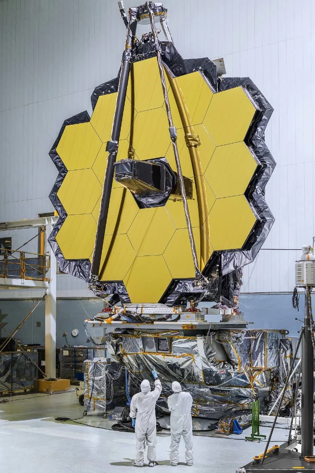 The 18-segment JWST primary mirror fully assembled at Goddard Space Flight Center in 2016, with two engineers in clean suits visible for scale