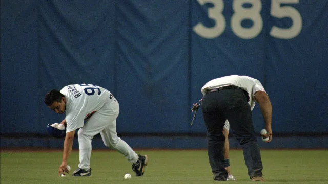 Grounds crew members collect souvenir baseballs from the Dodger Stadium field while players wait.