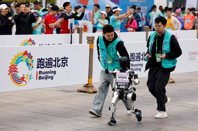A humanoid robot runs near a Beijing half-marathon course with event staff