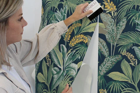 A person smoothing peel-and-stick wallpaper onto a living room accent wall using a squeegee