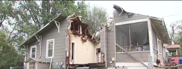 A house with a section of its roof torn open, exposing rafters, after a tree came down on it