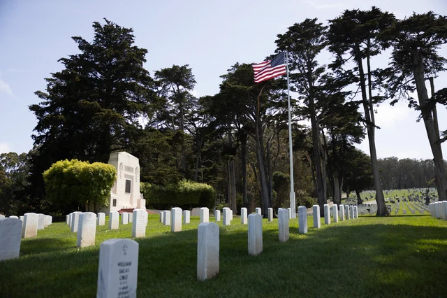 San Francisco National Cemetery at the Presidio — rows of white headstones extending to the horizon, American flag in the foreground, San Francisco Bay and Golden Gate Bridge in the background