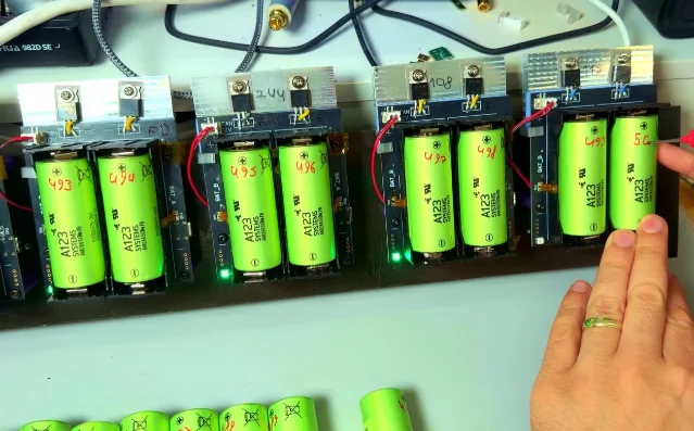 Five dual-cell tester boards connected to bright green cylindrical LFP cells, with heatsinks, wiring, and status LEDs visible on a workbench.