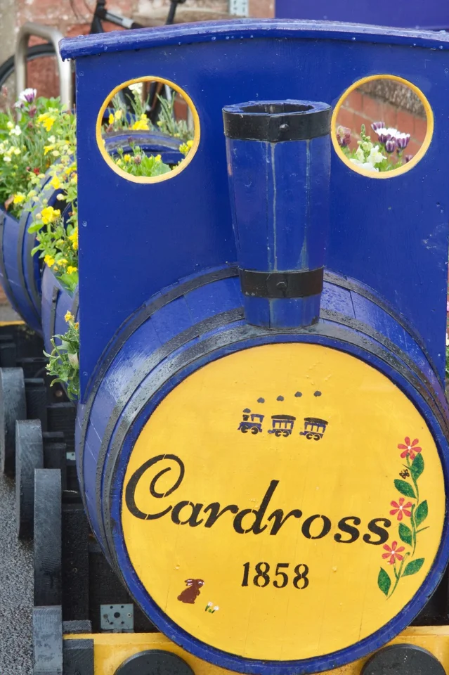 A blue and yellow steam-train-shaped planter on a station platform, its cab filled with flowers