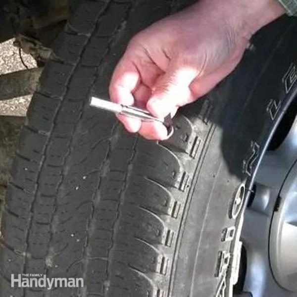 A hand holding a pocket tread-depth gauge flat against a car tire's tread, with the pin resting in a groove