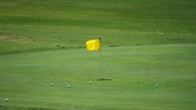 Golf course green with yellow flag and golf balls under a clear blue sky