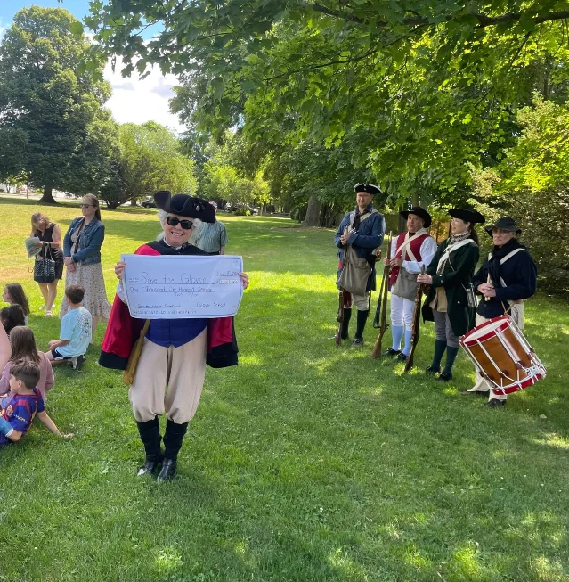 A student-made preservation check is presented outdoors with reenactors standing behind it