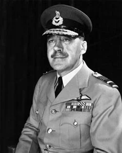 A black and white portrait of a moustached officer in a light uniform with a peaked cap