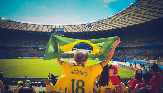 Brazil fans in a packed stadium showing the Brazilian flag and yellow kit