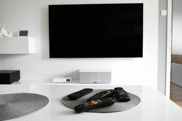 A wall-mounted television above a table holding four remote controls