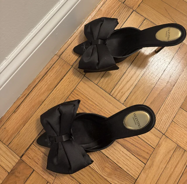 Valentino black satin bow-detail mule heels on a wood floor — a pick from the NET-A-PORTER 2nd markdown sale at up to 60% off