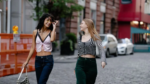 Two women in cropped street-style tops on a cobblestone city street