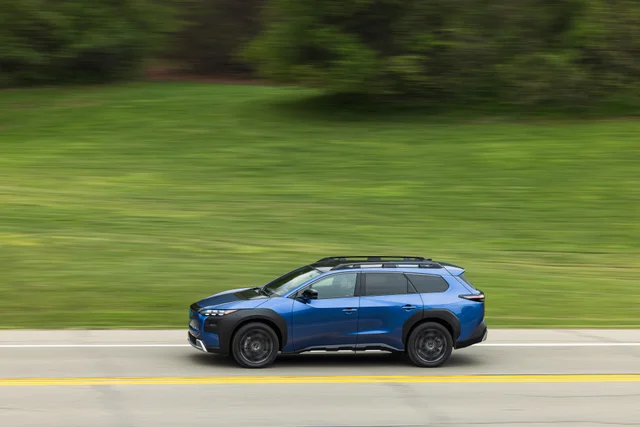 A blue Subaru Solterra electric SUV driving along a road, shot from the side with the background streaked by motion