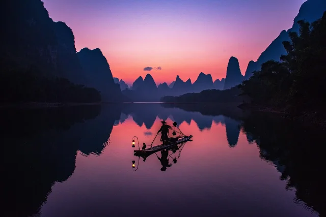 漓江夕阳,渔夫撑竹筏,两岸喀斯特山峰倒映水中,如水墨画