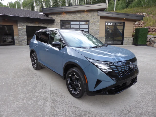 A blue 2027 Nissan Rogue Hybrid parked in front of a modern house