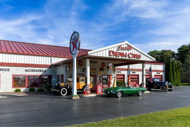 A white clapboard building with a red roof dressed as a vintage Texaco filling station, with classic cars parked beneath the canopy