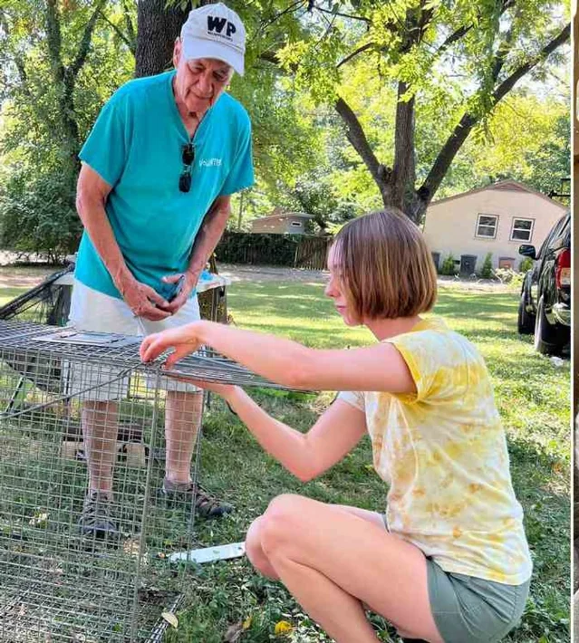 Jerry Vandiver and a helper kneeling beside a wire trap in a leafy suburban yard