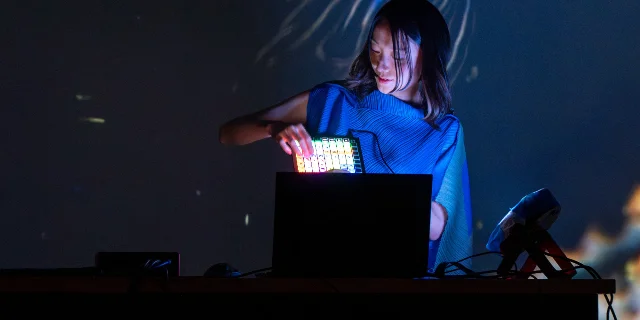 A performer operates a glowing biological controller in front of blue ocean projections
