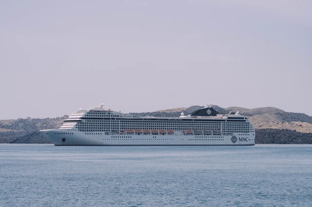 White cruise ship sailing on calm sea against a scenic coastline