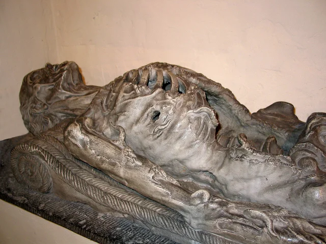 A carved stone tomb figure of a reclining man, his body partly eaten away and covered with carved worms