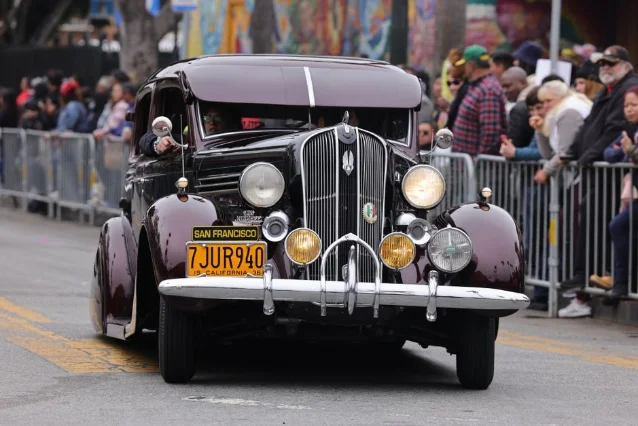 Vintage car rolling through a San Francisco street parade with spectators lining the barricades on both sides