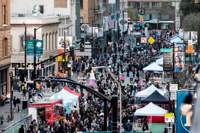 Outdoor street block party in San Francisco with dense crowd between buildings, white vendor tents lining the street