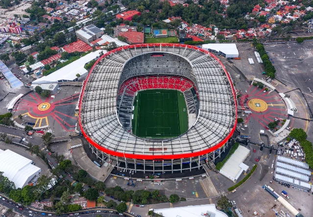 Aerial view of Mexico City Stadium (Estadio Banorte, formerly Estadio Azteca), showing the iconic oval arena surrounded by stands and the Mexico City skyline.