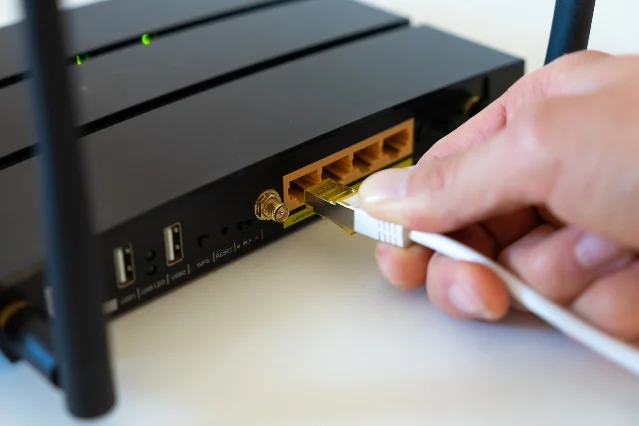 A hand plugging an Ethernet cable into a wireless router