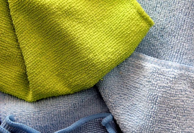 A hand pressing a grey microfiber cloth flat against a pale surface