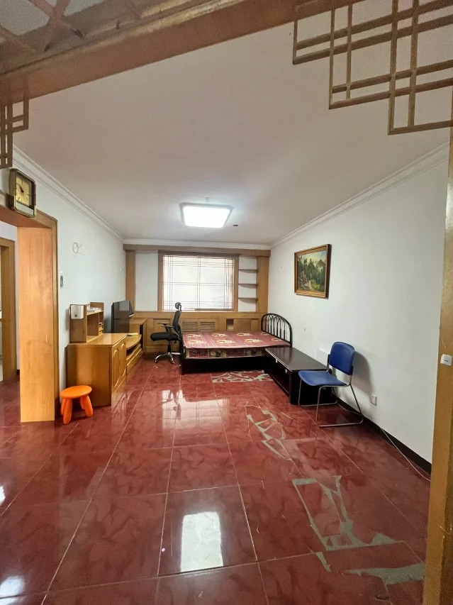 客厅全景,能看到红色地砖、床、书桌和简易家具