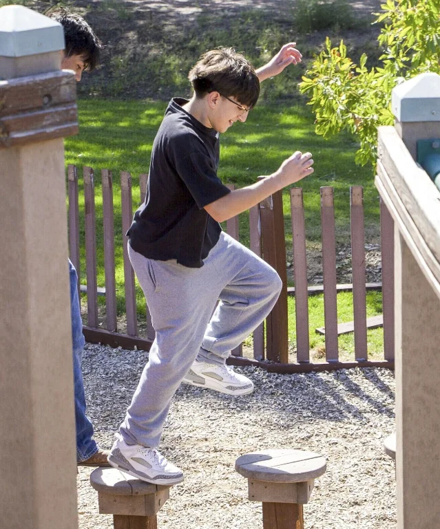 A teenager mid-jump between round wooden stump steps on a playground