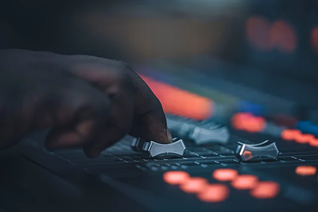 A hand adjusting faders on a mixing console — the slider metaphor for denoising strength control across different AI tools