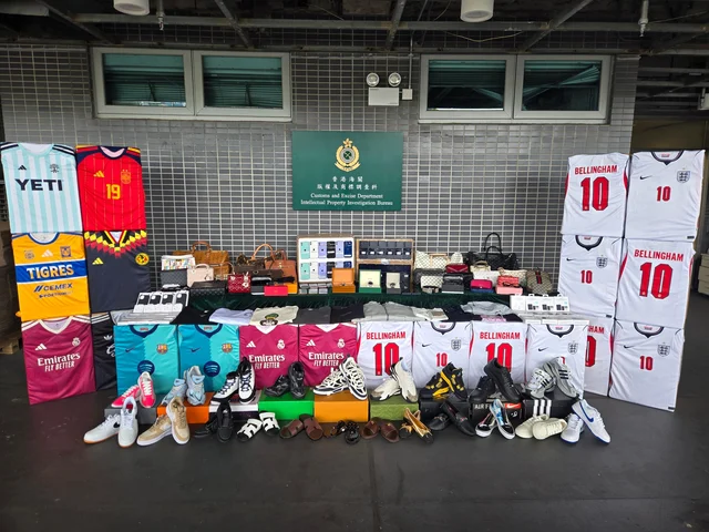 Display of seized counterfeit football shirts, handbags, shoes and watches in front of a Hong Kong Customs sign