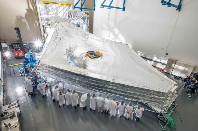 The JWST sunshield test unit deployed and stacked at Northrop Grumman's Redondo Beach facility in 2014, showing the five layers and the pink-purple silicon coating on the two outermost Sun-facing layers