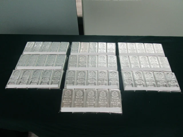 Rows of one-kilogram silver bars stamped with a palm-tree mark on a dark green table