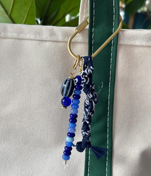 Beaded bag charm with blue and white glass/ceramic beads and gold carabiner, hanging on a white canvas tote bag