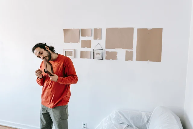 A person checks a wall arrangement with paper templates before hanging framed art.