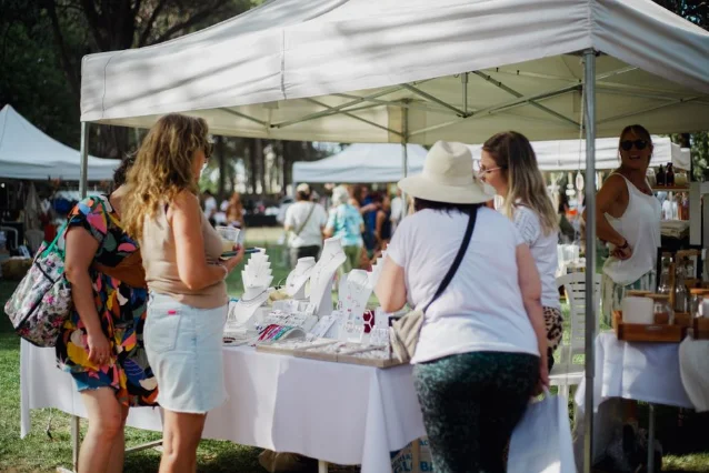 Visitors browse handmade jewelry and artisan goods at a sunny outdoor craft fair