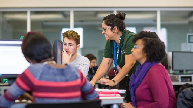 A teacher helping students work at computers in a classroom