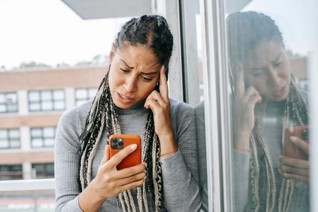 Woman standing on a balcony, looking at her phone, lost in thought