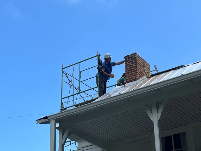 A volunteer works near the chimney on the Settlers Museum roof