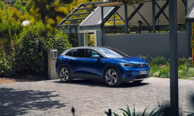 A blue Volkswagen ID.4 plugged into a wall-mounted charger outside a modern house
